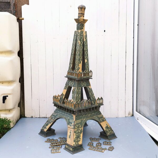 Rare jouet Tour eiffel en bois à construire en trois D composée de 36 pièces, datant de début XXème. Jeux en bois avec papier collé pour les motifs de la Tour, de la célèbre maison HV & W ( Henri Villard et Jules Weill) à Strasbourg , transférée à Luneville après guerre et devenu Majolu. Spécialistes de la fabrication de jouets en bois , solides et durables. Des manque de papiers sur des endroits, des petites casses de bois. Bel état compte tenu de son age mais reste dans jus. Hauteur : 127 cm Largeurs Pieds : 58 cm