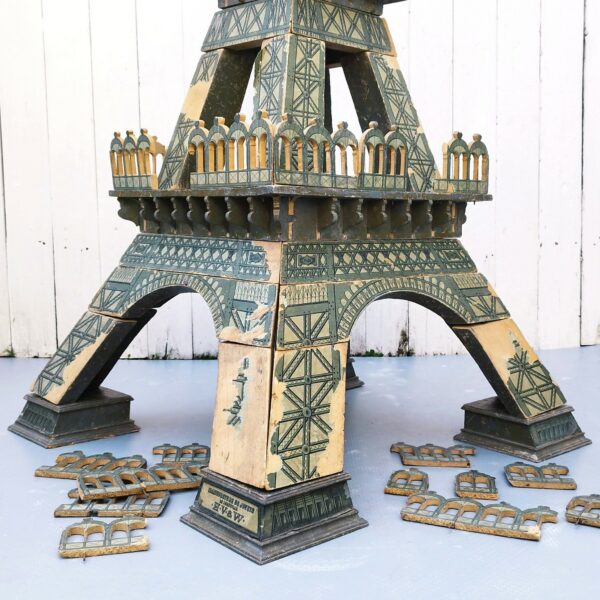 Rare jouet Tour eiffel en bois à construire en trois D composée de 36 pièces, datant de début XXème. Jeux en bois avec papier collé pour les motifs de la Tour, de la célèbre maison HV & W ( Henri Villard et Jules Weill) à Strasbourg , transférée à Luneville après guerre et devenu Majolu. Spécialistes de la fabrication de jouets en bois , solides et durables. Des manque de papiers sur des endroits, des petites casses de bois. Bel état compte tenu de son age mais reste dans jus. Hauteur : 127 cm Largeurs Pieds : 58 cm