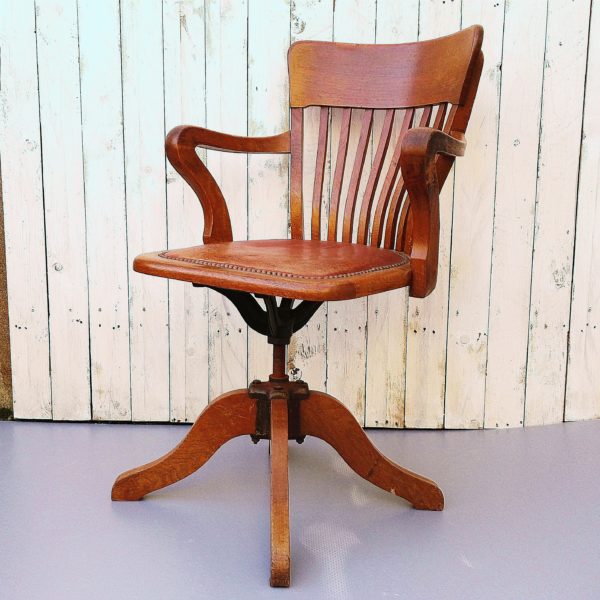 Fauteuil américain pivotant en bois et assise en cuir, datant des années 30, réglable en hauteur. Support d'assise en fonte et pieds en bois ainsi qu'un système de blocage à la hauteur maximum.