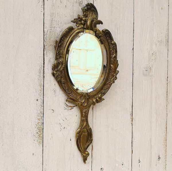 Miroir, face à main en bronze à décor rocaille, de style Louis XV. Epais miroir biseauté. Peut se suspendre au mur grâce à sont accroche de fixation sur l'arrière. Une décoloration sur le haut du miroir et rayures d'usage. Bon état. Longueur : 30 cm Largeur : 12,5 cm