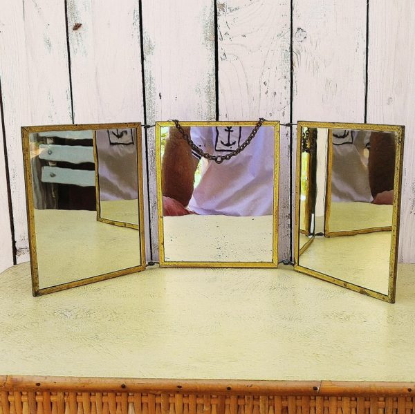 Miroir triptyque de barbier datant des années 50. La bordure est en métal doré, une chaînette permet de le suspendre. Décor de scènes galantes sur l'arrière quand il est fermé.  Un décor est piqué,et taché, abimé, l'autre décor est jauni,taché (il suffirait de les remplacer par un décor de votre choix). La bordure en métal doré est usée par endroit. Les deux miroirs extérieurs sont en très bon état et le miroir central est piqué. Dans son jus Dimensions d'un miroir : 15,5 x 19 cm Dimensions déployé : 50,5 x 19 cm
