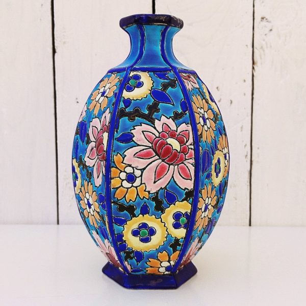 Vase en céramique de Longwy, à décor floral émaillé fait à la main. Cachet de la manufacture sur le dessous. De forme hexagonale. Un morceau du col a été cassé et bien recollé.  Bon état général. Hauteur : 18,5 cm