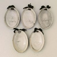 Lot de cinq médaillons en céramique datant des années 50-60, représentant des demoiselles au style et coiffures de cette époque. Chaque médaillons possèdent un noeud en velours noir et une accroche sur l'arrière pour les suspendre au mur. Elégants et romantiques. Signature sur l'arrière. Une micro égrenure sur deux médaillons. Très bon état. Dimensions : 12 x 8,5 cm