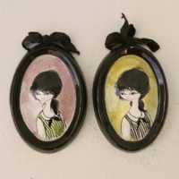 Lot de cinq médaillons en céramique datant des années 50-60, représentant des demoiselles au style et coiffures de cette époque. Chaque médaillons possèdent un noeud en velours noir et une accroche sur l'arrière pour les suspendre au mur. Elégants et romantiques. Signature sur l'arrière. Une micro égrenure sur deux médaillons. Très bon état. Dimensions : 12 x 8,5 cm