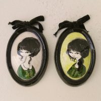 Lot de cinq médaillons en céramique datant des années 50-60, représentant des demoiselles au style et coiffures de cette époque. Chaque médaillons possèdent un noeud en velours noir et une accroche sur l'arrière pour les suspendre au mur. Elégants et romantiques. Signature sur l'arrière. Une micro égrenure sur deux médaillons. Très bon état. Dimensions : 12 x 8,5 cm