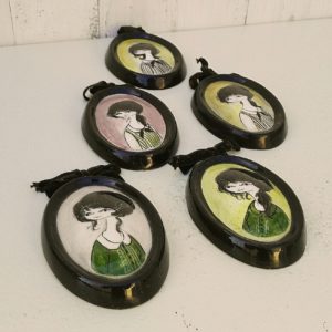 Lot de cinq médaillons en céramique datant des années 50-60, représentant des demoiselles au style et coiffures de cette époque. Chaque médaillons possèdent un noeud en velours noir et une accroche sur l'arrière pour les suspendre au mur. Elégants et romantiques. Signature sur l'arrière. Une micro égrenure sur deux médaillons. Très bon état. Dimensions : 12 x 8,5 cm