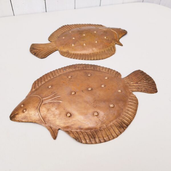 Deux poissons vénitiens en cuivre représentant une plie, décoration murale vintage. Un trou sur le haut pour les accrocher au mur. Petites rayures et traces d'usage. Dimensions : 26 x 17 cm
