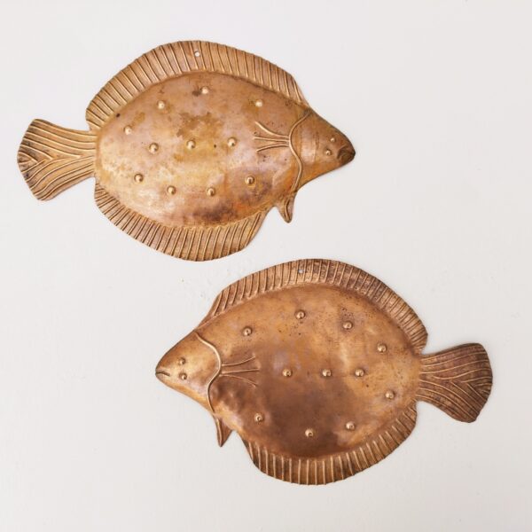 Deux poissons vénitiens en cuivre représentant une plie, décoration murale vintage. Un trou sur le haut pour les accrocher au mur. Petites rayures et traces d'usage. Dimensions : 26 x 17 cm