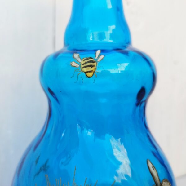 Bouteille ou vase soliflore de couleur bleue à décor émaillé d’angelots tirant sur un bandonéon devant le soleli, rehaussé d’une abeille sur le goulot. Trace de calcaire. Très bon état. Hauteur: 27, 5 cm.