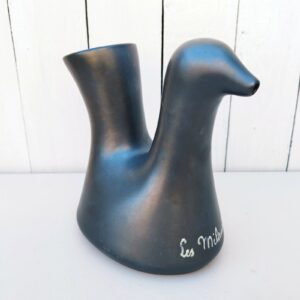 Pichet Cocotte en céramique noire irisée par  jean varoqueaux, sur une commande de l’actrice Joséphine Baker dans les années 60, pouvant servir de vase, de pichet ou en décoration. Il fut Produit dans le cadre d’une série de toutes les couleurs et créé pour être vendu au profit des enfants orphelins du château des milandes en Périgord noir. Inscription émaillée sur le pied : Les milandes Excellent état. Hauteur :  18,5 cm,