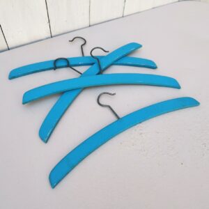 Lot de quatre cintres pour vêtements enfants, en bois peint en bleu. Peinture légèrement écaillée, traces d'usage. Traces de peinture rose sur le bas Bon état général. Longueur : 29 cm