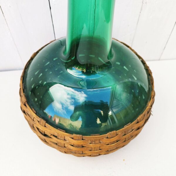 Vase en verre soufflé de couleur vert cerclé de lanière d'osier façon dame jeanne . Rayures d'usage sur le verre. Très bon état général. Hauteur : 48 cm Diamètre col : 7 cm Diamètre réceptacle : 25 cm