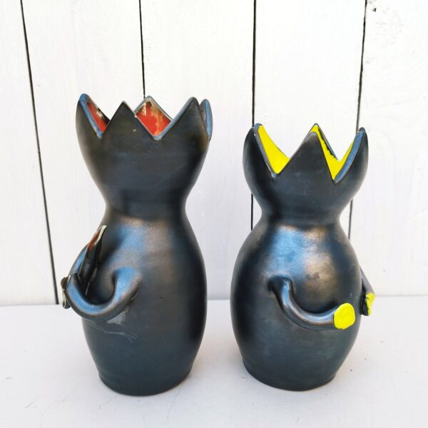 Paire de vases anthropomorphe faisant penser à des chats, en céramique noire avec intérieur jaune et l'autre rouge . Rappel de la couleur intérieur sur leurs mains. Le rouge tient une baguette. Manque un bout de la main du rouge. Très bon état. Hauteur jaune : 17,5 cm Hauteur Rouge : 19,5 cm