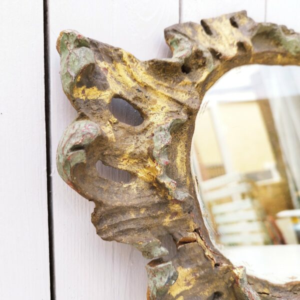 Miroir en bois doré de style baroque , de fabrication artisanale qui lui donne un vrai charme. Manque de dorure, des petits chocs et accrocs. Bon état général. Dimensions : 45 x 27 cm