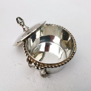 Boite à bijoux en métal argenté de la marque Lancel. Frise torsadée cordelette finissant par deux pompons. Signé Lancel sur le dessous. possède sa boite d'origine. Très bon état Hauteur avec couvercle : 10 cm Diamètre : 7,5 cm