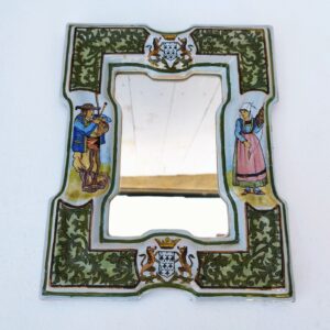 Miroir rectangulaire en faïence de Quimper, Porquier Beau . A décor d'un breton et une  bretonne dans un encadrement de rinceaux verts. Armoiries du duché de Bretagne en partie haute et basse. Un point d'accroche sur l'arrière avec velours de protection. Des défauts de cuisson et d'émaillage, des petites égrenures sans gravité. Très bon état. Dimensions : 27 x 22 cm