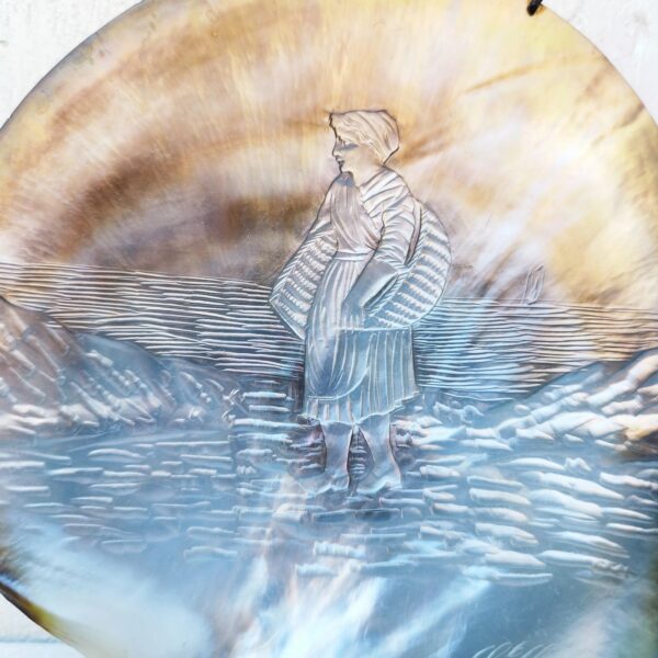 Coquillage nacre sculpté, à décor d'une pêcheuse à pied, souvenir de Saint Servan à coté de Saint-Malo. Possède le cerclage pour le suspendre. Très bon état général. dimensions : 12 x 11,5 cm