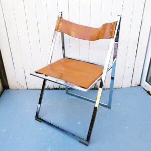 Paire chaises pliantes modèle "Elios" en métal chomé et cuir de couleur fauve datant de la fin des années 60, dessinées par Fontoni et Geraci. Manque un ressort sous l'une des chaises n'altérant pas la solidité de celle ci (ressort facilement trouvable sur internet). Quelques petits manque de chrome. Petites griffures sur le cuir. Bon état général Hauteur assise : 44,5 cm Hauteur totale : 82,5 cm Profondeur : 45 cm