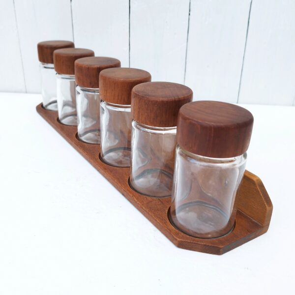 Série de six pots à épices en verre, avec support. Made in Denmark, design scandinave. Bouchon imitation bois à vis. Bon état général. Hauteur avec bouchon : 10 cm Diamètre col : 5 cm Longueur du support : 41 cm