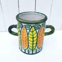 Vase ou pot à anse en céramique, à décor de feuilles colorées jaunes et orange. Un micro éclat sur le dessous, non visible une fois posé.  Très bon état.  Hauteur : 16 cm Diamètre : 12, 5 cm