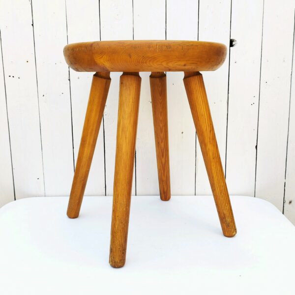 Tabouret vintage quadripode en pin. Assise creusée lui conférant un bon confort. Très belle patine du bois. Tabouret faisant penser au travail de Charlotte Perriand Traces et rayures d'usage. Bon état général. Hauteur : 46,5 cm Diamètre : 36,5 cm