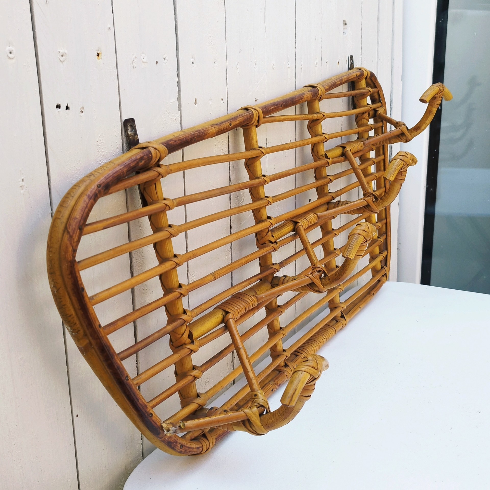 Grand porte-manteaux en rotin, 4 patères. Datant des années 60. Deux accroches murales. Manque un lien sur le coté gauche au niveau de la patère, a été refixé avec une pointe et collé. Bon état général. Longueur : 75 cm hauteur max : 40 cm Hauteur min : 30 cm