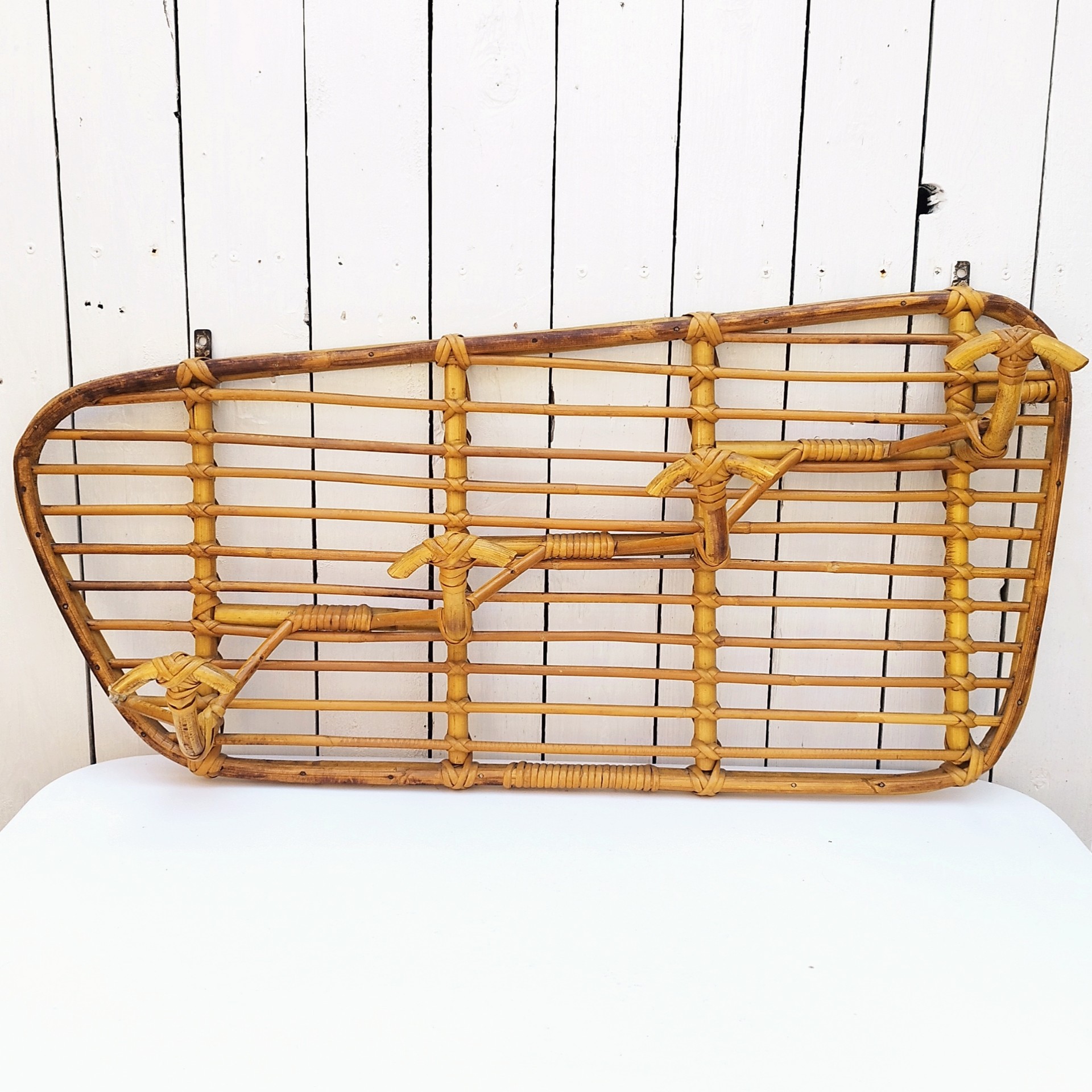 Grand porte-manteaux en rotin, 4 patères. Datant des années 60. Deux accroches murales. Manque un lien sur le coté gauche au niveau de la patère, a été refixé avec une pointe et collé. Bon état général. Longueur : 75 cm hauteur max : 40 cm Hauteur min : 30 cm