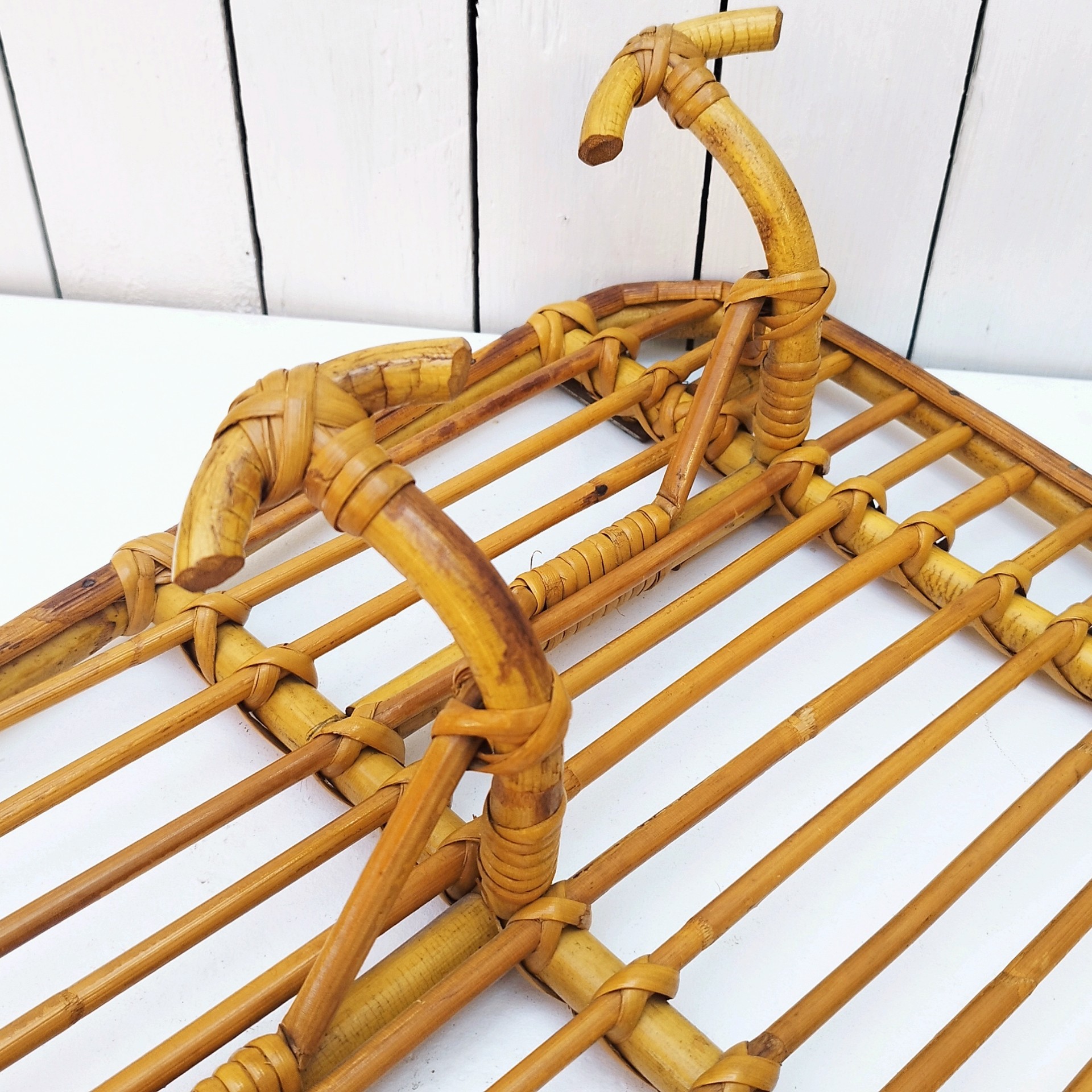 Grand porte-manteaux en rotin, 4 patères. Datant des années 60. Deux accroches murales. Manque un lien sur le coté gauche au niveau de la patère, a été refixé avec une pointe et collé. Bon état général. Longueur : 75 cm hauteur max : 40 cm Hauteur min : 30 cm
