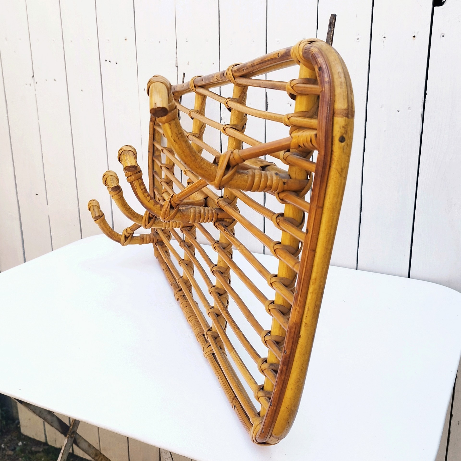 Grand porte-manteaux en rotin, 4 patères. Datant des années 60. Deux accroches murales. Manque un lien sur le coté gauche au niveau de la patère, a été refixé avec une pointe et collé. Bon état général. Longueur : 75 cm hauteur max : 40 cm Hauteur min : 30 cm