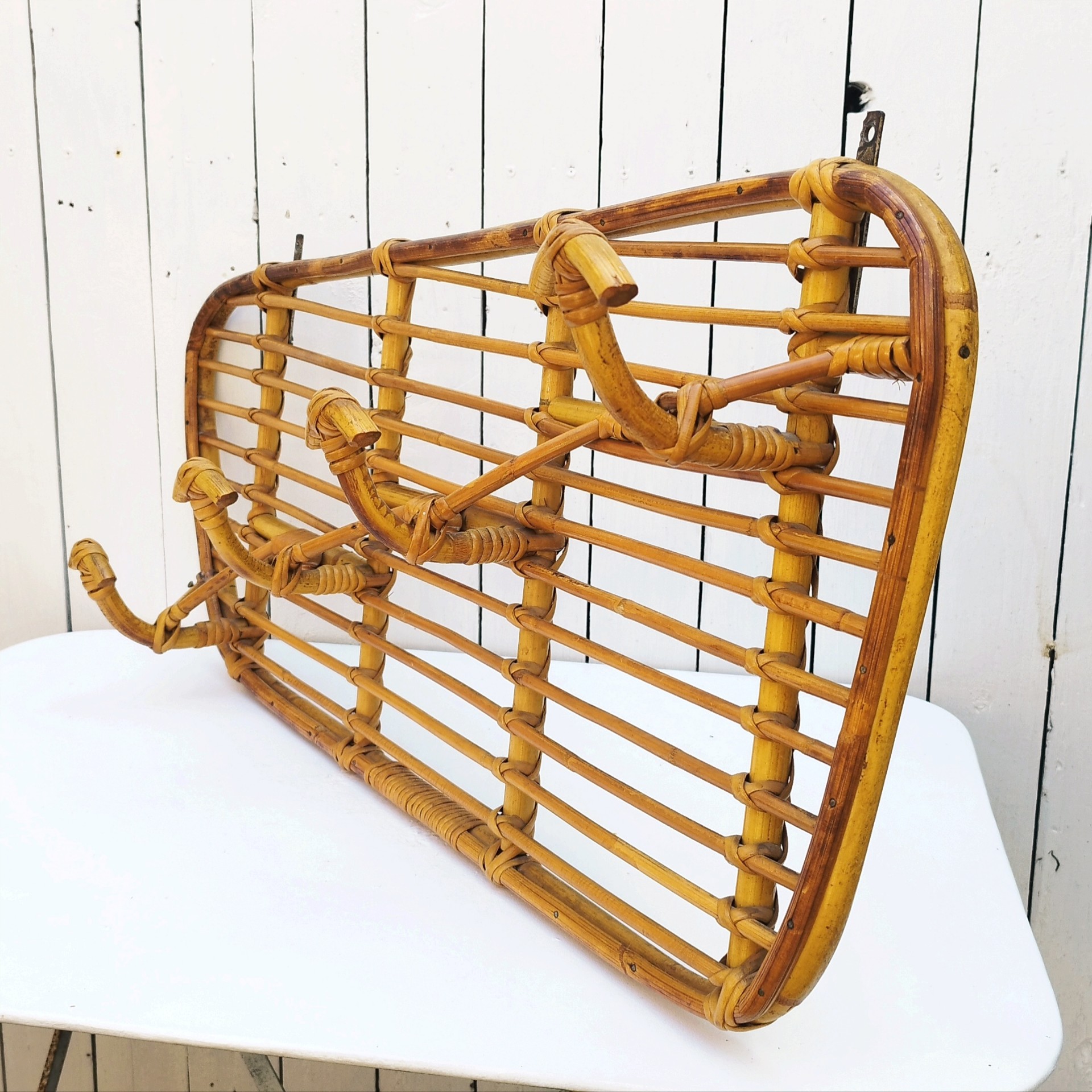 Grand porte-manteaux en rotin, 4 patères. Datant des années 60. Deux accroches murales. Manque un lien sur le coté gauche au niveau de la patère, a été refixé avec une pointe et collé. Bon état général. Longueur : 75 cm hauteur max : 40 cm Hauteur min : 30 cm