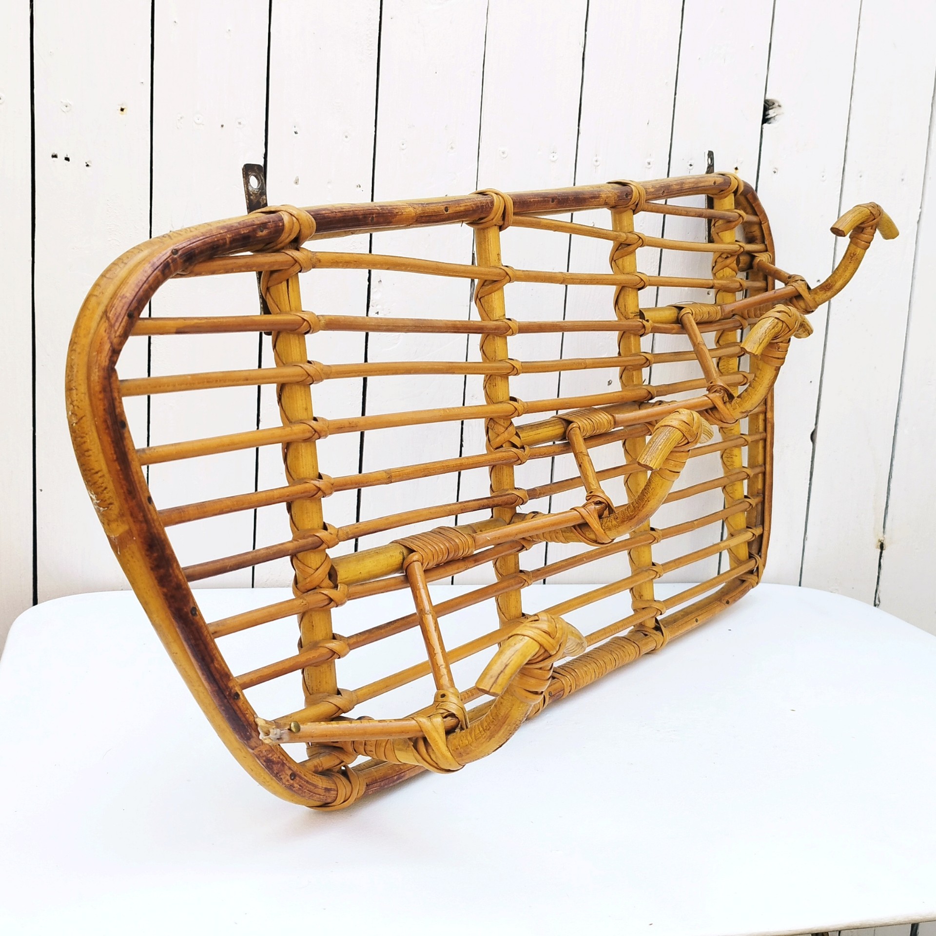 Grand porte-manteaux en rotin, 4 patères. Datant des années 60. Deux accroches murales. Manque un lien sur le coté gauche au niveau de la patère, a été refixé avec une pointe et collé. Bon état général. Longueur : 75 cm hauteur max : 40 cm Hauteur min : 30 cm