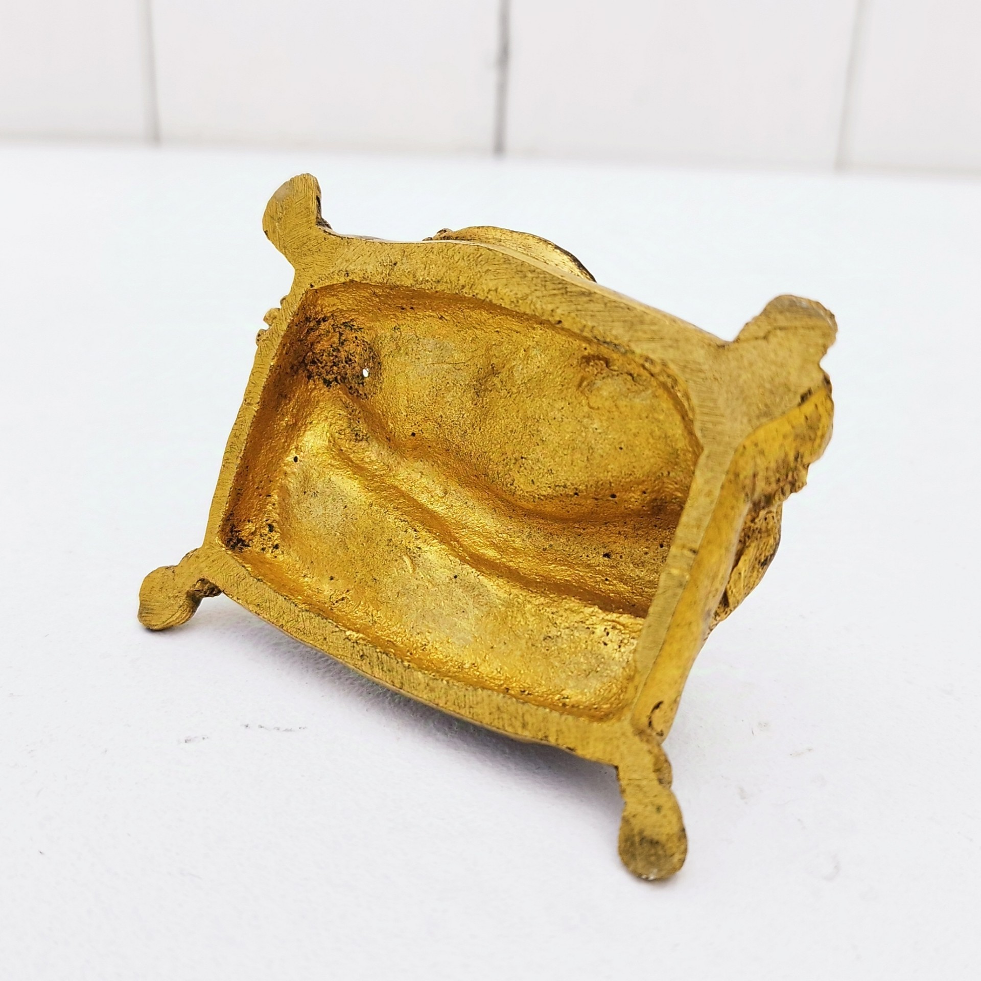 Petit bronze doré représentant un chien assis sur un coussin. quatre pieds représentant les pompons du coussin. Dorure usée par endroit. Bon état général. Dimensions :  7,5 x 5 x 5 cm