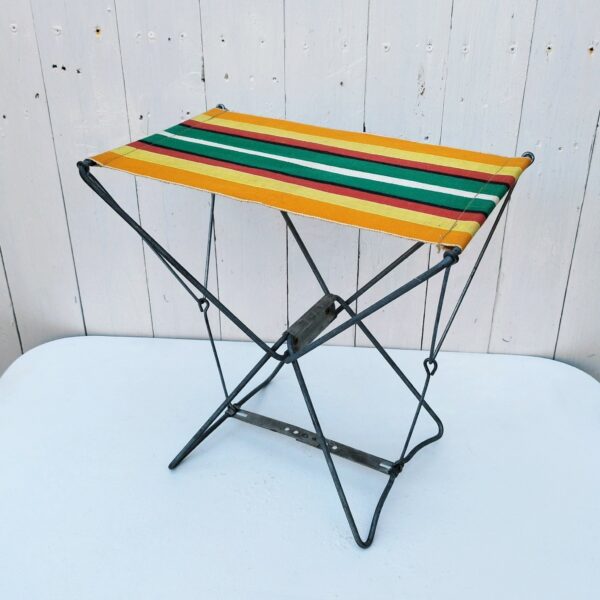 Tabouret d'appoint de camping ou siège de plage datant des années 70. Structure en métal et assise en toile de couleur. Une icône des années 70. Petites trace de corrosion, traces d'usage. Bon état général Hauteur : 35 cm Dimensions assise : 35 x 24 cme