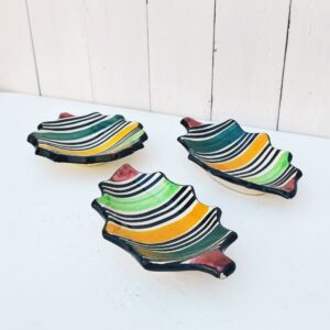 Trois coupelles en céramique de Vallauris, décor rayures de différentes couleurs. Deux coupelle en forme de feuilles, et une en étoile. Une micro égrenure sur l'étoile, un petit éclat sur le bout d'une feuille et un petit éclat sur le bout et la queue de l'autre feuille. Non visible une fois posées. Bon état général. Dimensions feuilles : 20 x 11 cm Diamètre étoile : 13 cm
