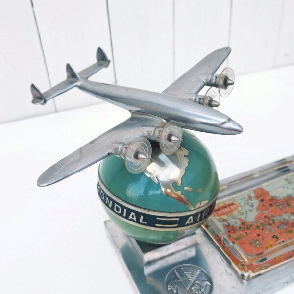 Rare authentique cendrier prestige Air France globe avec Constellation en fonte d'aluminium peinte, vers 1950. Représentant un Lockheed Constellation survolant un globe terrestre avec un cendrier en verre décoré d'un mappemonde par Lucien Boucher.  Globe cerclé du message " Air France - Réseau aérien mondial" Socle décoré du logo Air France hippocampe moulé dans la masse, globe peint (peinture jaunie sur la partie basse du globe, à cause de la fumée de cigarette) .  Constellation avec hélices à double rayures. Marqué Made in France sur le socle à l'arrière du globe. Décor de la mappemonde du cendrier écaillé sur le contour, traces d'usage sur le socle, patins en caoutchouc noir tous présents et en bon état. Ensemble en très bon état d'origine. Hauteur : ~17 cm Longueur : 24,4 cm Profondeur : 12,8 cm Constellation : 21 x 17 cm