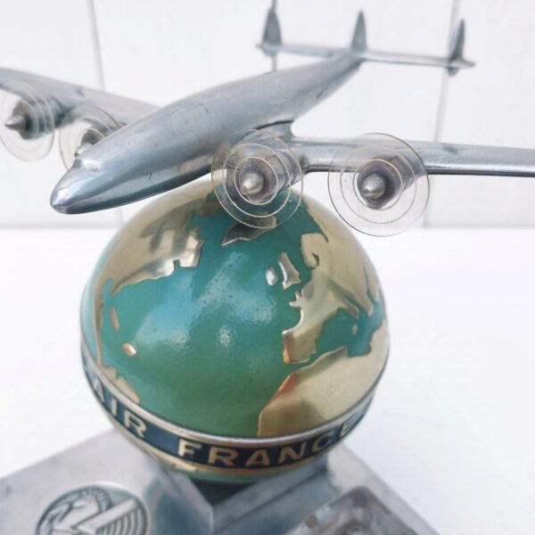 Rare authentique cendrier prestige Air France globe avec Constellation en fonte d'aluminium peinte, vers 1950. Représentant un Lockheed Constellation survolant un globe terrestre avec un cendrier en verre décoré d'un mappemonde par Lucien Boucher.  Globe cerclé du message " Air France - Réseau aérien mondial" Socle décoré du logo Air France hippocampe moulé dans la masse, globe peint (peinture jaunie sur la partie basse du globe, à cause de la fumée de cigarette) .  Constellation avec hélices à double rayures. Marqué Made in France sur le socle à l'arrière du globe. Décor de la mappemonde du cendrier écaillé sur le contour, traces d'usage sur le socle, patins en caoutchouc noir tous présents et en bon état. Ensemble en très bon état d'origine. Hauteur : ~17 cm Longueur : 24,4 cm Profondeur : 12,8 cm Constellation : 21 x 17 cm