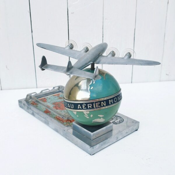 Rare authentique cendrier prestige Air France globe avec Constellation en fonte d'aluminium peinte, vers 1950. Représentant un Lockheed Constellation survolant un globe terrestre avec un cendrier en verre décoré d'un mappemonde par Lucien Boucher.  Globe cerclé du message " Air France - Réseau aérien mondial" Socle décoré du logo Air France hippocampe moulé dans la masse, globe peint (peinture jaunie sur la partie basse du globe, à cause de la fumée de cigarette) .  Constellation avec hélices à double rayures. Marqué Made in France sur le socle à l'arrière du globe. Décor de la mappemonde du cendrier écaillé sur le contour, traces d'usage sur le socle, patins en caoutchouc noir tous présents et en bon état. Ensemble en très bon état d'origine. Hauteur : ~17 cm Longueur : 24,4 cm Profondeur : 12,8 cm Constellation : 21 x 17 cm