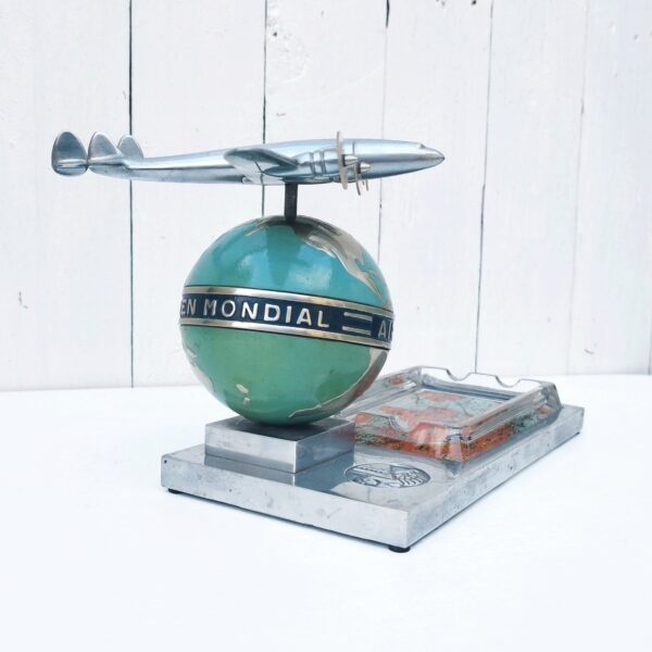 Rare authentique cendrier prestige Air France globe avec Constellation en fonte d'aluminium peinte, vers 1950. Représentant un Lockheed Constellation survolant un globe terrestre avec un cendrier en verre décoré d'un mappemonde par Lucien Boucher.  Globe cerclé du message " Air France - Réseau aérien mondial" Socle décoré du logo Air France hippocampe moulé dans la masse, globe peint (peinture jaunie sur la partie basse du globe, à cause de la fumée de cigarette) .  Constellation avec hélices à double rayures. Marqué Made in France sur le socle à l'arrière du globe. Décor de la mappemonde du cendrier écaillé sur le contour, traces d'usage sur le socle, patins en caoutchouc noir tous présents et en bon état. Ensemble en très bon état d'origine. Hauteur : ~17 cm Longueur : 24,4 cm Profondeur : 12,8 cm Constellation : 21 x 17 cm