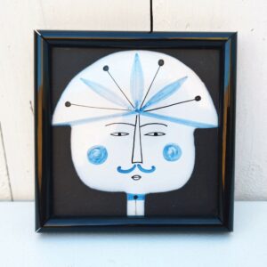 Carreau en céramique représentant un personnage, par Roger Capron à Vallauris. Encadrement noir avec un point d'accroche sur l'arrière. Très bon état. Dimensions : 10,5 x 10,5 cm