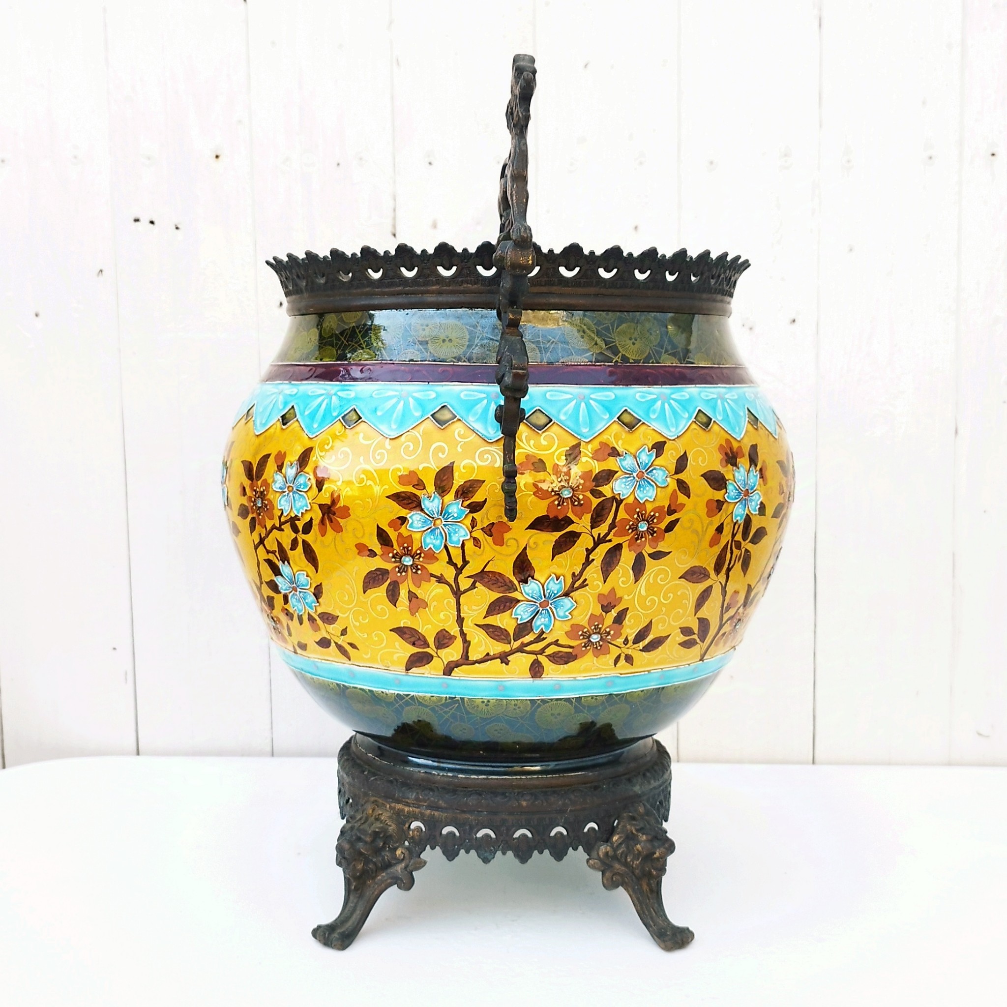 Grand cache-pot ou jardinière en céramique de Sarreguemines numéro 2048. Cerclé d'une couronne en bronze aux prises formant des lions. Pied tripodes en bronze. Couleurs bien vives. races d'usage à l'intérieur. Très bon état. Hauteur max  : 40 cm Diamètre : 25 cm