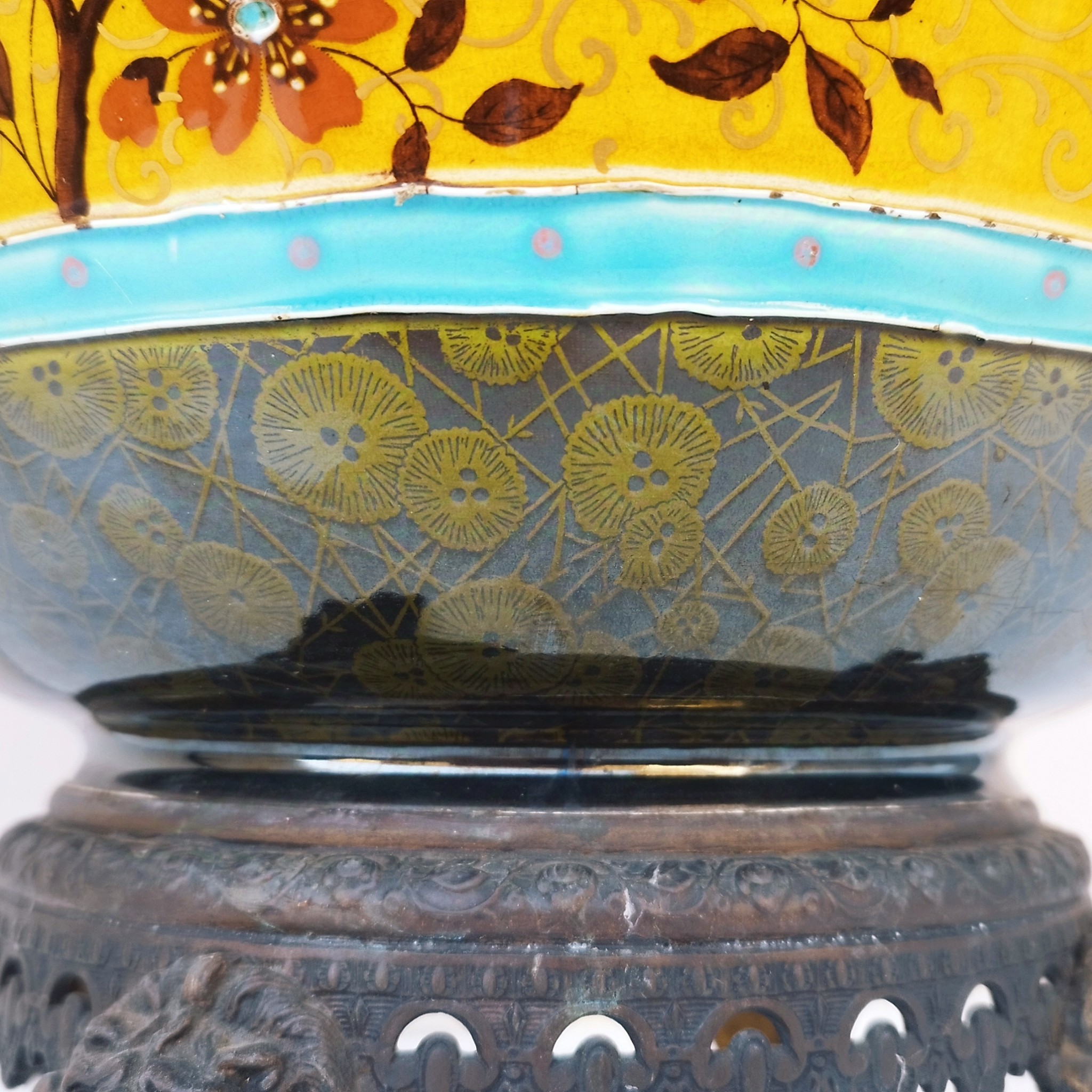 Grand cache-pot ou jardinière en céramique de Sarreguemines numéro 2048. Cerclé d'une couronne en bronze aux prises formant des lions. Pied tripodes en bronze. Couleurs bien vives. races d'usage à l'intérieur. Très bon état. Hauteur max  : 40 cm Diamètre : 25 cm