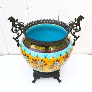 Grand cache-pot ou jardinière en céramique de Sarreguemines numéro 2048. Cerclé d'une couronne en bronze aux prises formant des lions. Pied tripodes en bronze. Couleurs bien vives. races d'usage à l'intérieur. Très bon état. Hauteur max  : 40 cm Diamètre : 25 cm