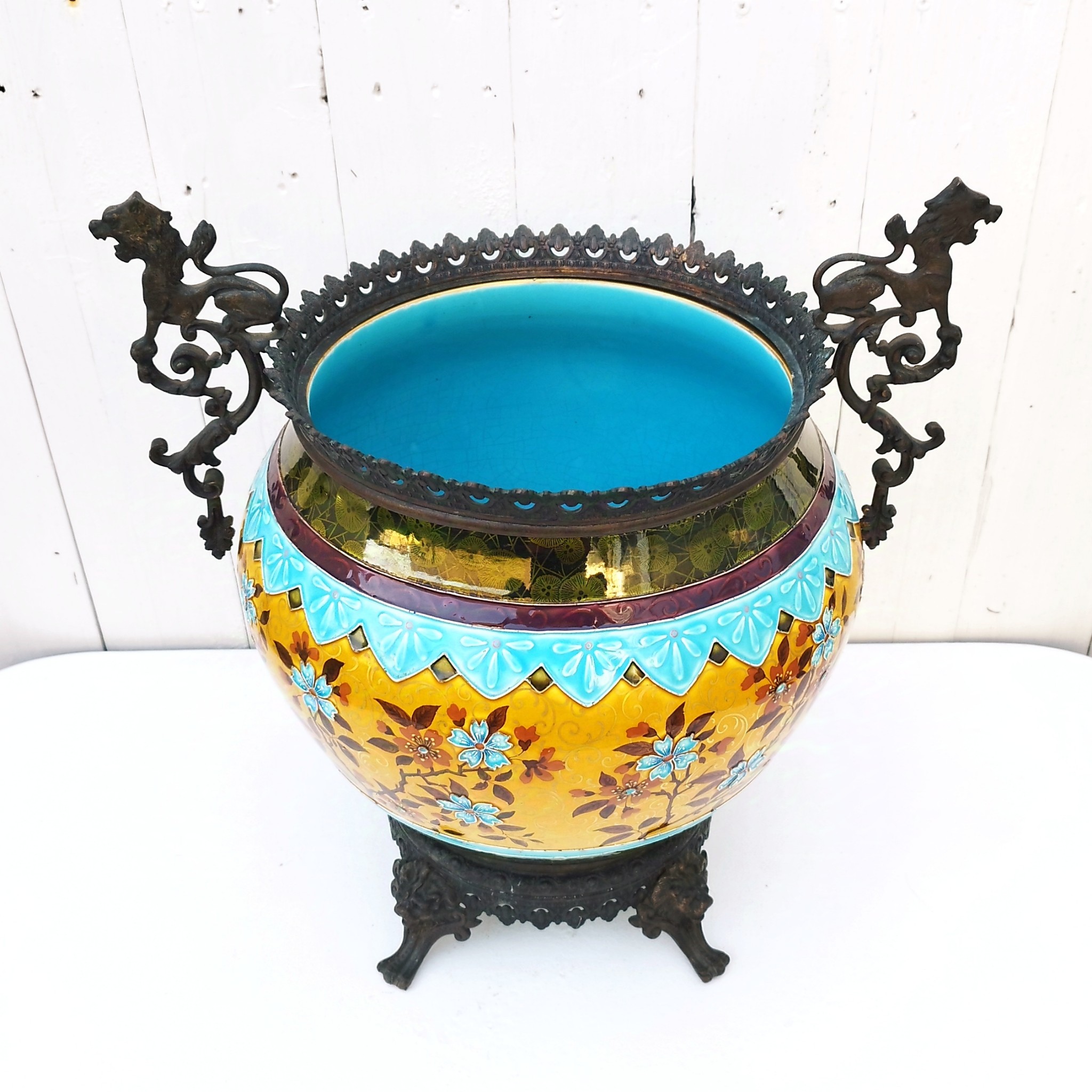 Grand cache-pot ou jardinière en céramique de Sarreguemines numéro 2048. Cerclé d'une couronne en bronze aux prises formant des lions. Pied tripodes en bronze. Couleurs bien vives. races d'usage à l'intérieur. Très bon état. Hauteur max  : 40 cm Diamètre : 25 cm