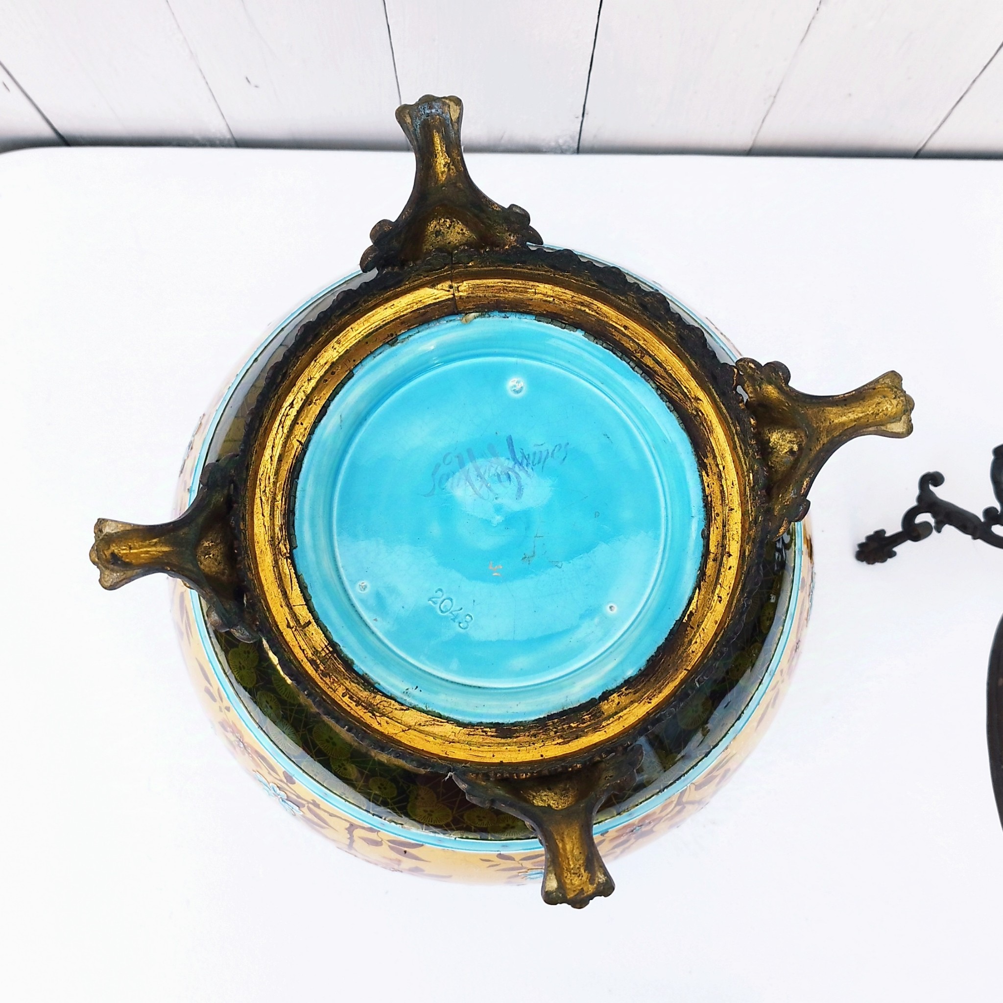 Grand cache-pot ou jardinière en céramique de Sarreguemines numéro 2048. Cerclé d'une couronne en bronze aux prises formant des lions. Pied tripodes en bronze. Couleurs bien vives. races d'usage à l'intérieur. Très bon état. Hauteur max  : 40 cm Diamètre : 25 cm