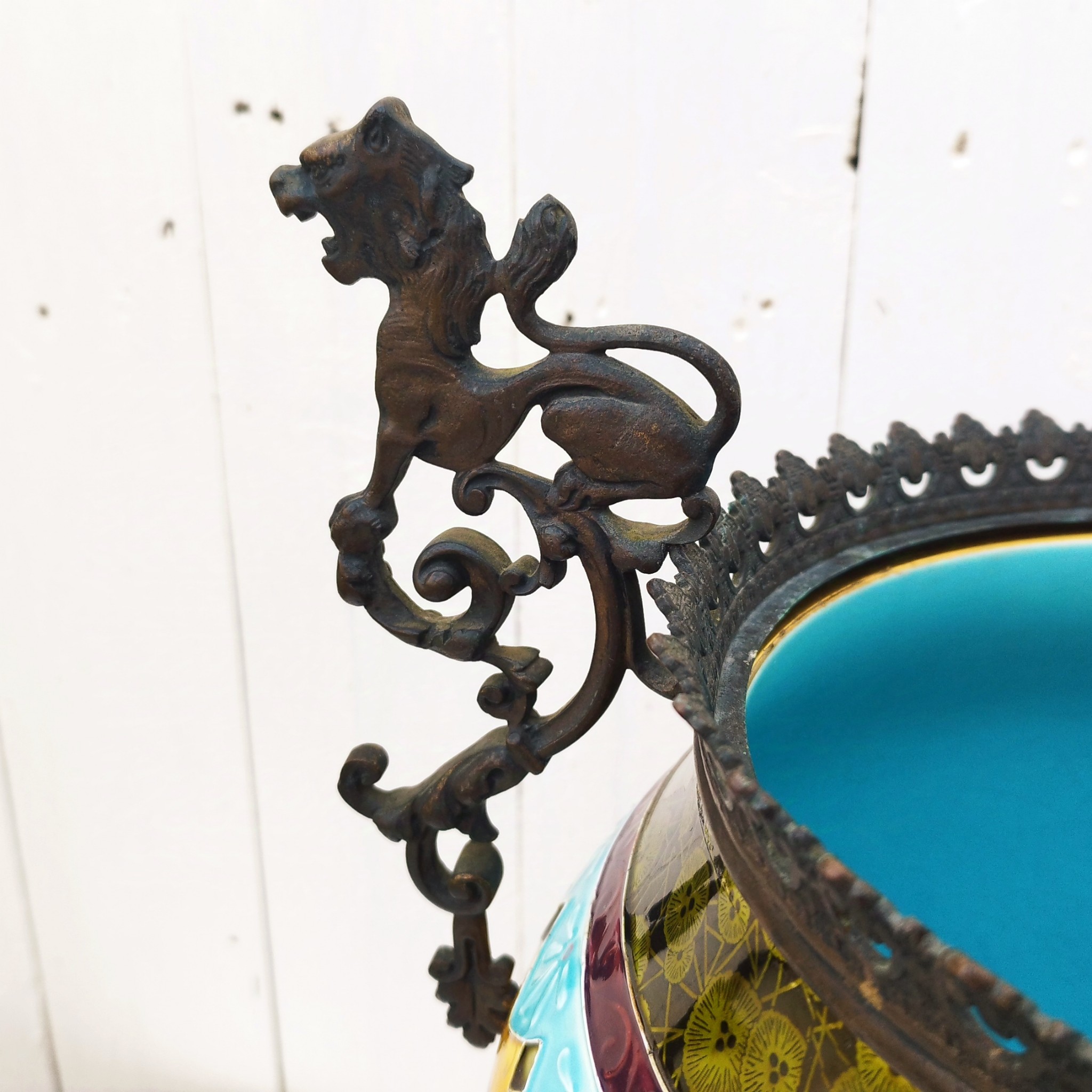 Grand cache-pot ou jardinière en céramique de Sarreguemines numéro 2048. Cerclé d'une couronne en bronze aux prises formant des lions. Pied tripodes en bronze. Couleurs bien vives. races d'usage à l'intérieur. Très bon état. Hauteur max  : 40 cm Diamètre : 25 cm