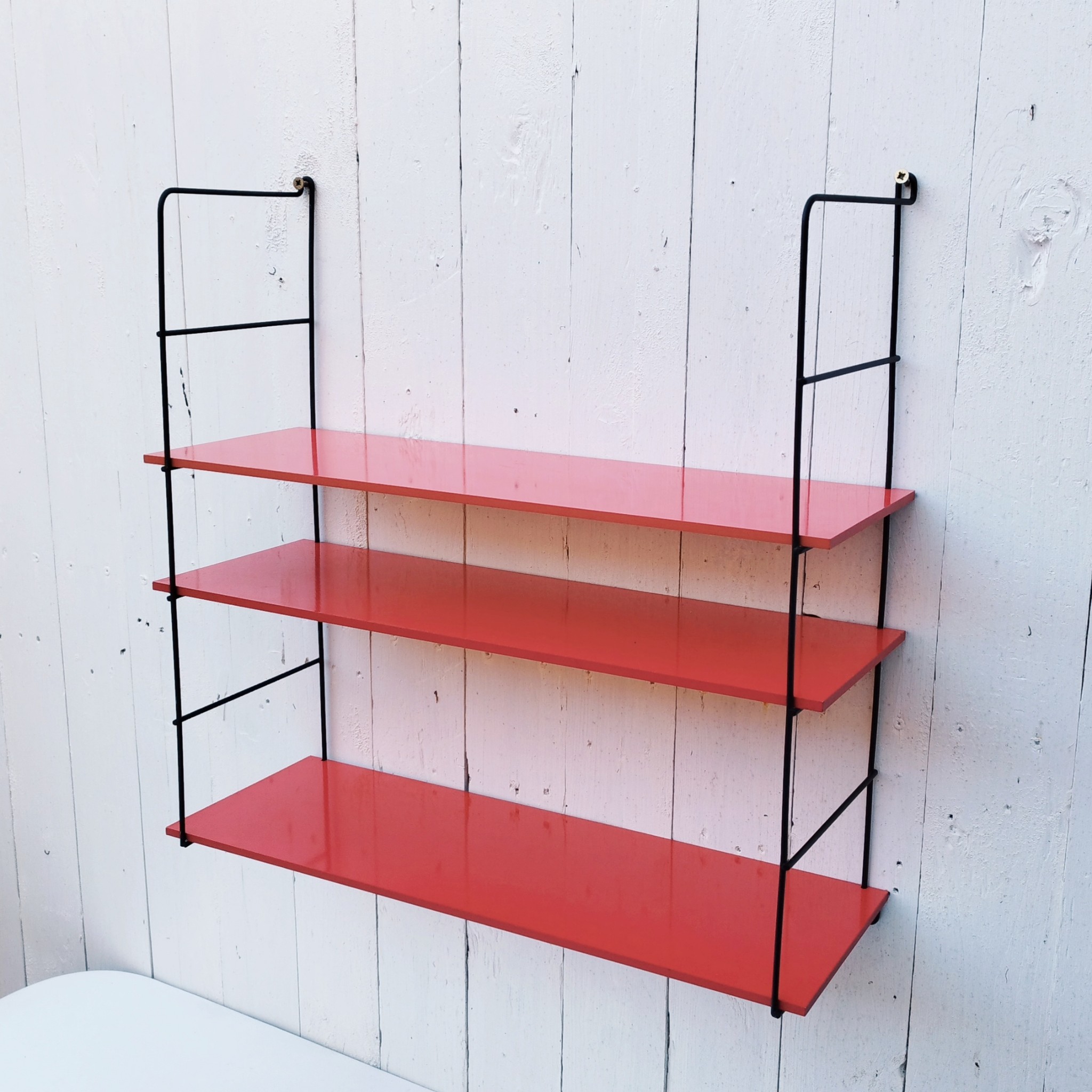 Etagère murale style string, montants en métal noir et étagères en mélaminé de couleur rouge. Petites rayures et taches sur les étagères, petites traces de corrosion sur les montants. Un montant légèrement tordu. Très bon état Hauteur : 52 cm Dimensions étagères : 52,5 x 17 cm