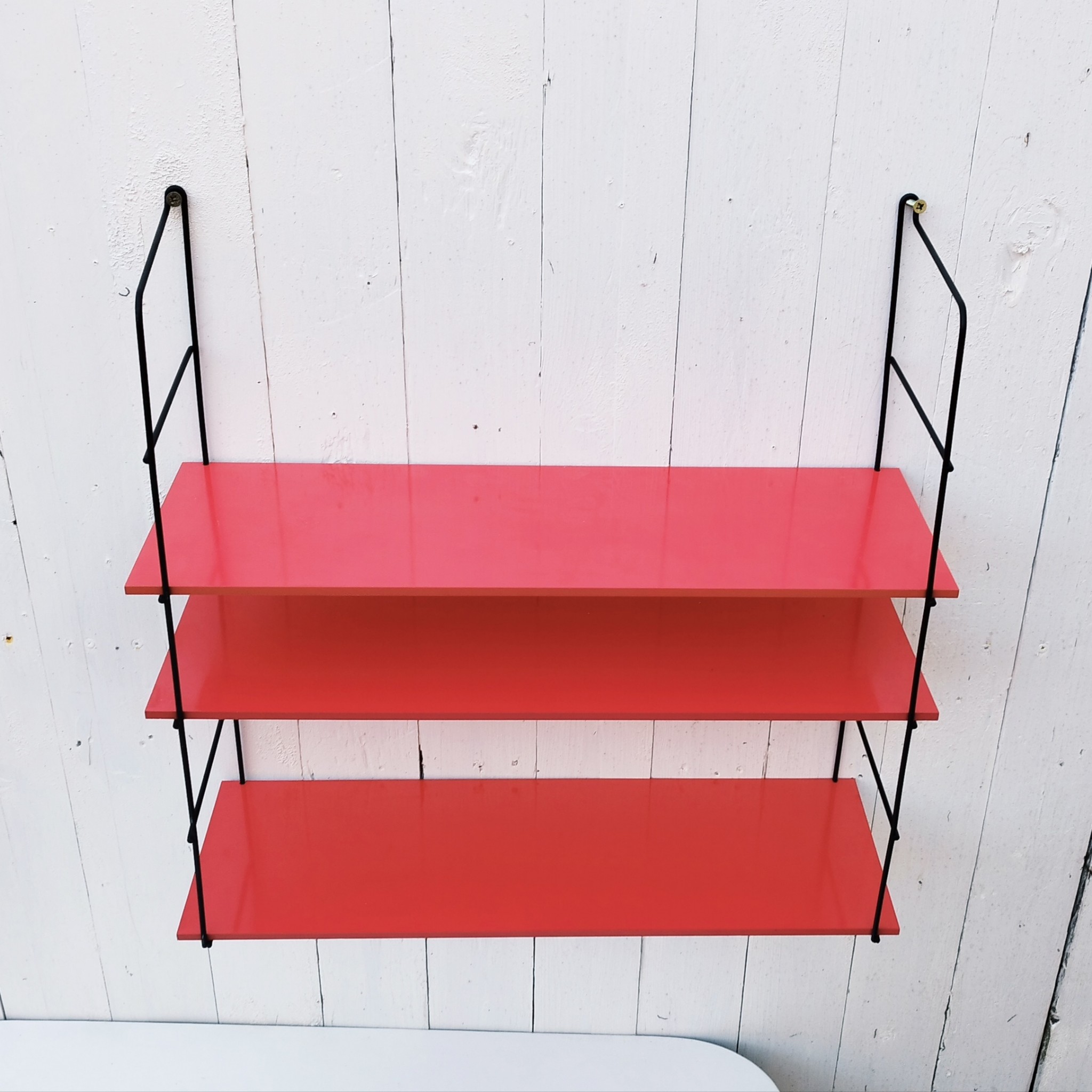 Etagère murale style string, montants en métal noir et étagères en mélaminé de couleur rouge. Petites rayures et taches sur les étagères, petites traces de corrosion sur les montants. Un montant légèrement tordu. Très bon état Hauteur : 52 cm Dimensions étagères : 52,5 x 17 cm