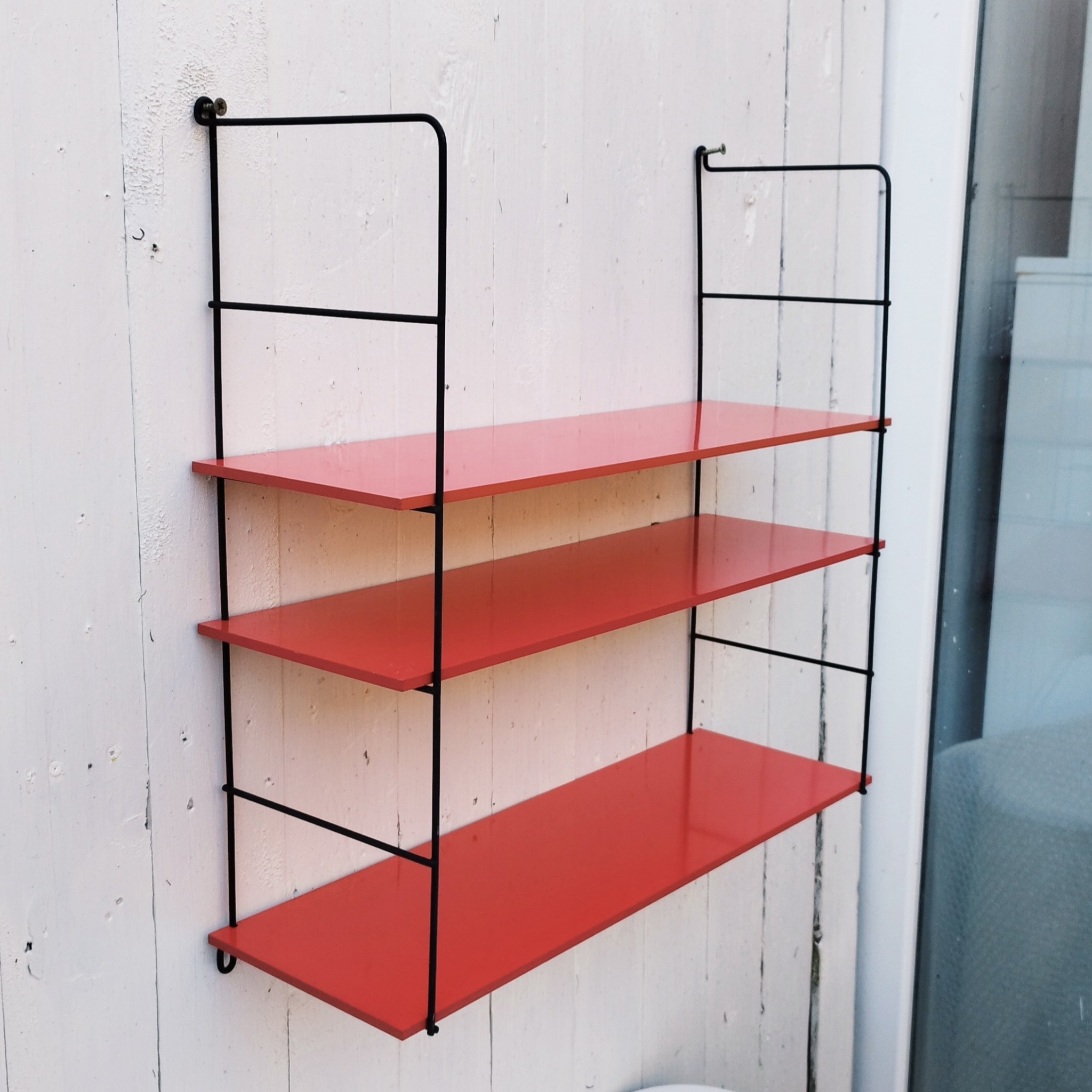 Etagère murale style string, montants en métal noir et étagères en mélaminé de couleur rouge. Petites rayures et taches sur les étagères, petites traces de corrosion sur les montants. Un montant légèrement tordu. Très bon état Hauteur : 52 cm Dimensions étagères : 52,5 x 17 cm