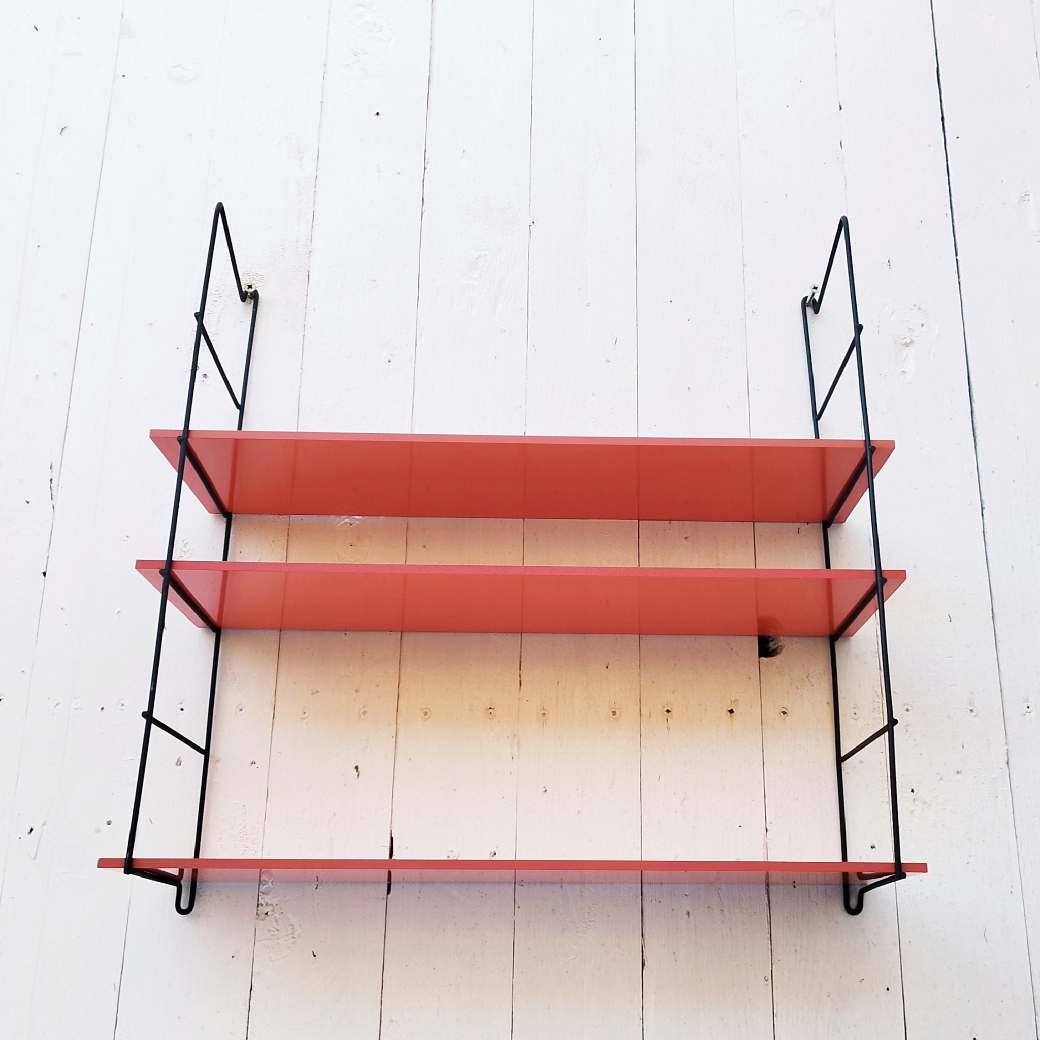 Etagère murale style string, montants en métal noir et étagères en mélaminé de couleur rouge. Petites rayures et taches sur les étagères, petites traces de corrosion sur les montants. Un montant légèrement tordu. Très bon état Hauteur : 52 cm Dimensions étagères : 52,5 x 17 cm