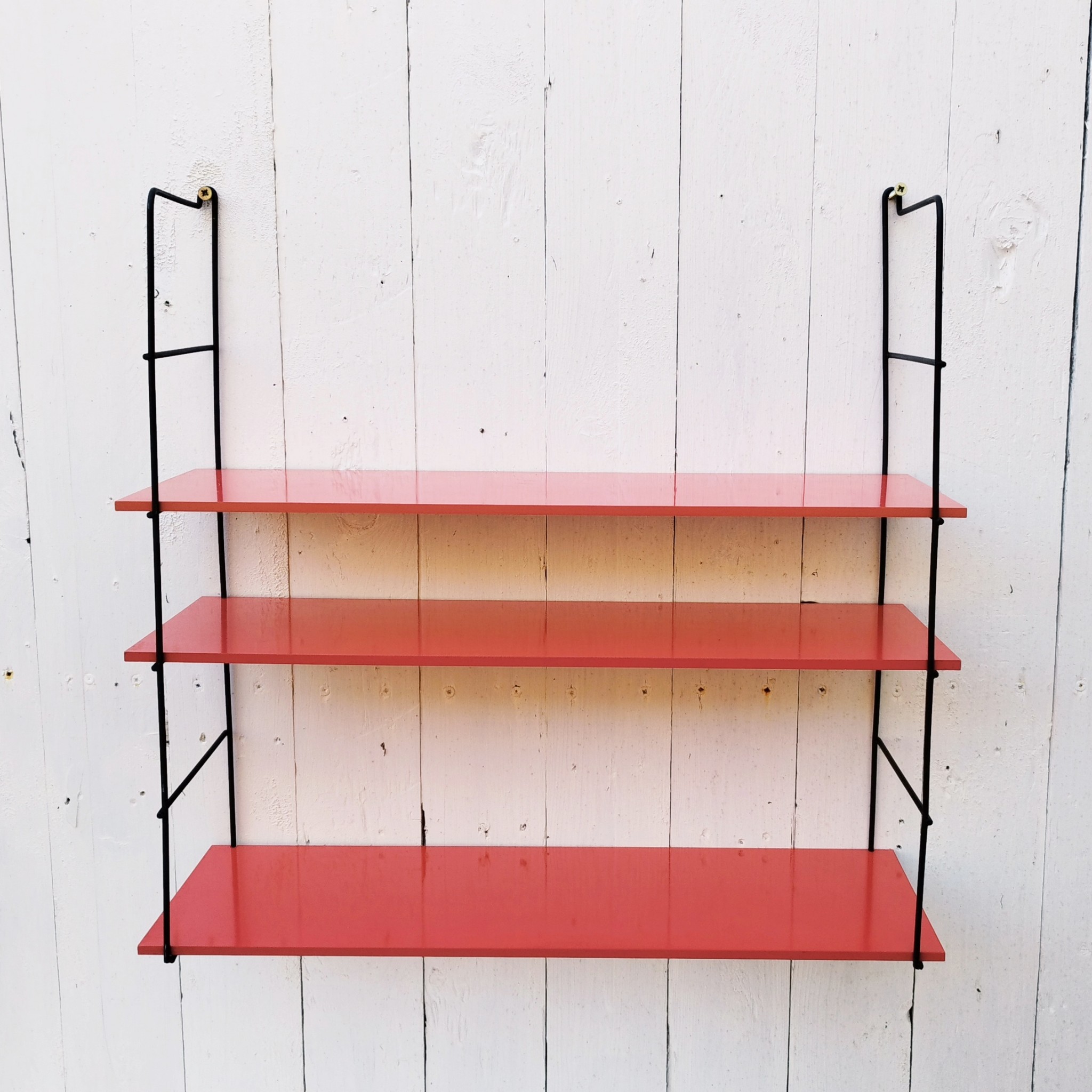 Etagère murale style string, montants en métal noir et étagères en mélaminé de couleur rouge. Petites rayures et taches sur les étagères, petites traces de corrosion sur les montants. Un montant légèrement tordu. Très bon état Hauteur : 52 cm Dimensions étagères : 52,5 x 17 cm